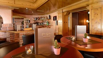 A stylish restaurant with wooden walls and round tables. Small plants and menus are on the tables.