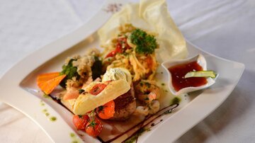 An artistically arranged plate with various dishes, including fish, shrimp, and vegetables. Accompanied by a sauce and fresh herbs.