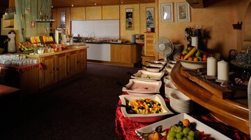 An inviting breakfast room with a buffet full of fresh fruits. In the background, various foods and drinks are arranged on wooden furniture.