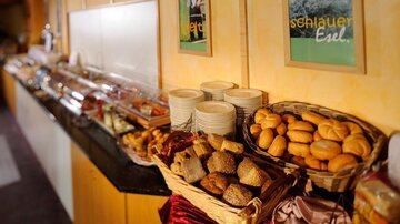 A rich breakfast buffet featuring various types of bread and pastries. In the background, numerous delicacies and dishes can be seen.
