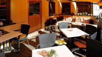 A cozy outdoor area with tables and chairs in a restaurant. The walls are designed in warm colors, and there are comfortable seating options.