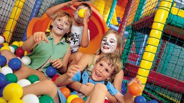 Four children are happily playing in a ball pit. They are laughing and having a lot of fun in a colorful play environment.