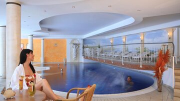 An elegant wellness area with an indoor pool and loungers. A woman is relaxing with a drink in her hand.