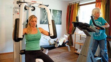 A woman is working out on a fitness machine, while another woman is jogging on a treadmill. In the background, you can see a bright and friendly environment.