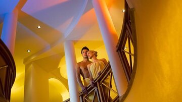 A couple stands on an elegant staircase with soft lighting in warm colors. The atmosphere is romantic and inviting.