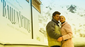 A couple stands in front of a building named "BallunSpitze" in the snow. The two appear happy and are enjoying the winter atmosphere.