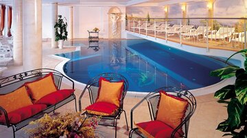 A stylish indoor pool with cozy seating areas and decorative cushions. Light-flooded space with a relaxing ambiance.