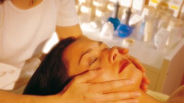 A woman is receiving a facial massage at a beauty studio. She looks relaxed as another person gently places their hands on her face.