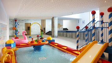 A colorful, enclosed water area with slides and play equipment for children. There are inflatable toys and a sparkling pool.