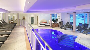A modern indoor pool with comfortable loungers and a relaxing atmosphere. Soft lighting and large windows create an inviting environment.
