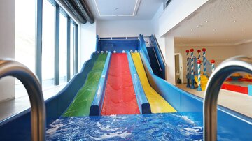 An indoor water park with several water slides in bright colors. In the foreground, the water pool located beneath the slides is visible.