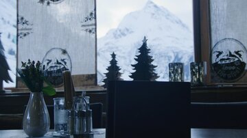 A cozy restaurant with a view of snow-covered mountains. A flower vase and spice shakers are on the table.