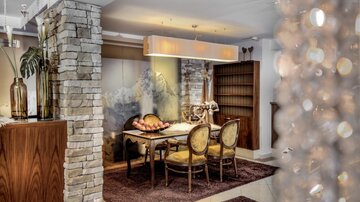 Ein eleganter Essbereich mit einem Holztisch und gemütlichen Stühlen. Die Wände sind teilweise mit Stein verkleidet, und die Beleuchtung sorgt für eine warme Atmosphäre.