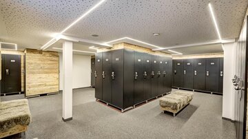 Ein modernes Umkleideraum mit schwarzen Schließfächern und gemütlichen Sitzgelegenheiten. Die Beleuchtung ist hell und schafft eine einladende Atmosphäre.