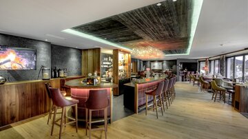 Eine elegante Bar mit Holzinterieur und einer gemütlichen Atmosphäre. Helle Beleuchtung und ein Kamin sorgen für einladendes Flair.