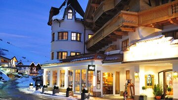 Ein charmantes Hotel in den Bergen, umgeben von Schnee. Das Gebäude hat eine rustikale Architektur und leuchtet sanft in der Abenddämmerung.