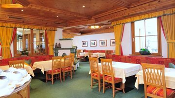 Ein einladendes Restaurant mit Holzmobiliar und bunten Vorhängen. Die Tische sind dekoriert und laden zum Essen ein.