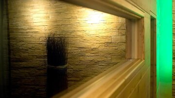 Eine moderne Wand mit Steinoptik und sanfter Beleuchtung. Im Vordergrund ist ein dekoratives Element aus trockenen Zweigen zu sehen.