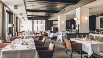 Ein elegantes Restaurant mit gedeckten Tischen und modernen Stühlen. Die große Fensterfront sorgt für viel Tageslicht und eine einladende Atmosphäre. | © elizabeth.at