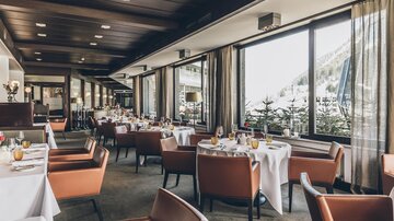 Ein elegantes Restaurant mit gemütlichen Sesseln und schön gedeckten Tischen. Große Fenster bieten einen Blick auf die umliegende Landschaft.