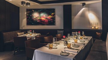 Ein elegantes Restaurant mit einem schön gedeckten Tisch. An der Wand hängt ein farbenfrohes Kunstwerk.
