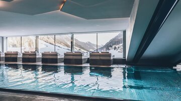 Ein eleganter Innenpool mit Blick auf schneebedeckte Berge. Gemütliche Liegen laden zum Entspannen ein. | © elizabeth.at