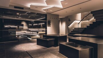 Ein modernes, elegantes Raumdesign mit minimalistischen Möbeln und sanfter Beleuchtung. Die stilvolle Treppe und die reflektierenden Oberflächen verleihen dem Raum eine ansprechende Atmosphäre. | © elizabeth.at