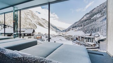 Ein modern eingerichteter Raum mit Blick auf ein schneebedecktes Tal. Die Umgebung zeigt Berge und ein kleines Dorf im Winter. | © elizabeth.at