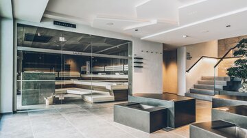 Ein moderner Wellnessbereich mit minimalistischer Einrichtung und gemütlichen Sitzgelegenheiten. Große Fenster lassen viel Licht herein und schaffen eine entspannte Atmosphäre. | © elizabeth.at