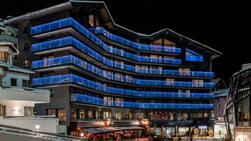 Ein modernes Gebäude mit blauen Lichtern erleuchtet die Nacht. Menschen bewegen sich auf der Straße in der Nähe des Eingangs.