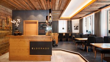 Ein modernes Restaurant mit einer warmen Holzdekor und stilvollem Empfangstresen. Tische und Stühle sind gemütlich angeordnet, um eine einladende Atmosphäre zu schaffen.