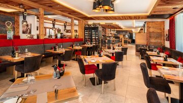 Ein modernes Restaurant mit Holzelementen und eleganten Tischdekorationen. Die Sitzbereiche sind gemütlich und einladend gestaltet.