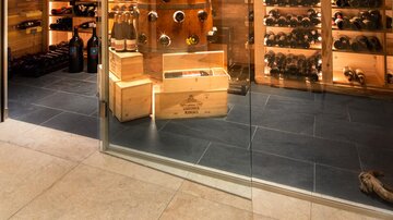 Ein eleganter Weinkeller mit holzverkleideten Regalen voller Weinflaschen. Die gläserne Tür ermöglicht einen Blick auf die sorgfältig angeordnete Sammlung.
