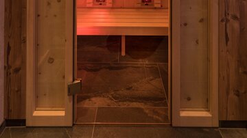 Eine Infrarotkabine mit Holzverkleidung und orangefarbigem Licht. Die Kabine ist bereit zur Nutzung und vermittelt eine warme, entspannende Atmosphäre.