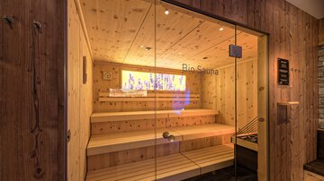 Eine moderne Bio-Sauna mit hellem Holzinterieur und Glasfront. Die Bänke laden zum Entspannen ein.
