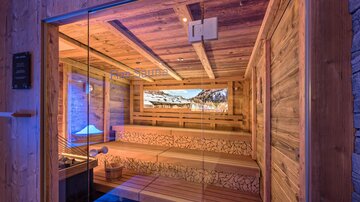 Eine moderne Sauna mit Holzinterieur und gemütlichen Bänken. Durch große Fenster kann man die schöne Berglandschaft beobachten.