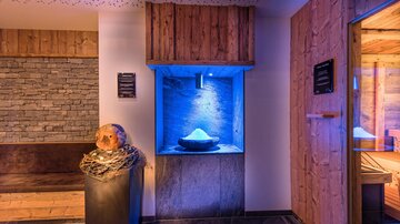 Ein stilvolles Wellnessambiente mit Holzverkleidungen und sanftem blauen Licht. Im Mittelpunkt steht ein dekorativer Brunnen mit Salzkristallen.