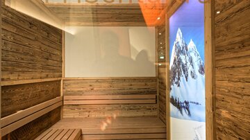Ein moderner Raum mit Holzelementen und einer Sauna-Bank. An der Wand befindet sich ein großes Bildschirm-Bild mit schneebedeckten Bergen.
