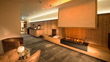 Ein gemütlicher Raum mit Holzverkleidung und einem modernen Kamin. Sofas und ein kleiner Tisch laden zum Entspannen ein.