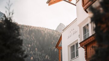 Ein charmantes Hotelgebäude in alpiner Umgebung. Im Hintergrund sind die Berge und ein Wald zu sehen.