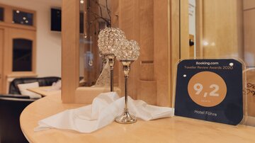 Ein eleganter Tisch mit gläsernen Kegel-Gläsern und einer Auszeichnung für das Hotel Föhre. Die Auszeichnung zeigt eine Bewertung von 9,2 auf Booking.com.