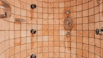 Eine moderne Dusche mit runden Wänden und Fliesen in warmen Farbtönen. Fünf Duschköpfe sind gleichmäßig verteilt.