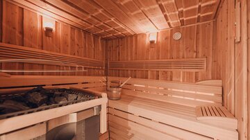 Eine gemütliche Sauna aus Holz mit Sitzbänken und einem Saunaofen. Das Raumlicht schafft eine entspannende Atmosphäre.