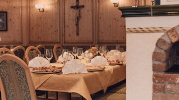 Ein gemütlicher Essbereich mit gedecktem Tisch und Faltservietten. Im Hintergrund sind Holzwände und eine hölzerne Kreuzdekoration sichtbar.