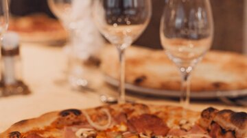 Eine köstliche Pizza mit verschiedenen Belägen auf einem Tisch. Im Hintergrund stehen Weingläser, die auf ein geselliges Essen hinweisen.