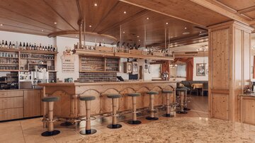 Eine gemütliche Bar mit Holzelementen und Barhockern. Die Umgebung ist hell und einladend.