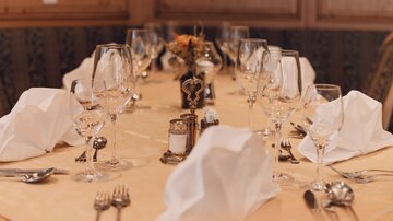 Ein elegant gedeckter Tisch mit Weingläsern und Stoffservietten. In der Mitte steht eine kleine Blumendekoration.