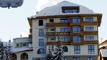 A modern hotel with wooden cladding in a snow-covered mountain area. In the background, clear blue skies and snow can be seen.