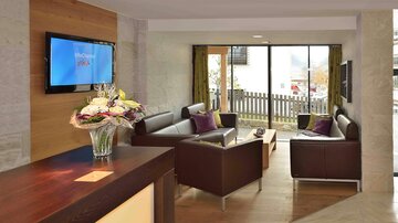 A modern reception area with comfortable armchairs and a television on the wall. Large windows let in plenty of light and offer a view outside.