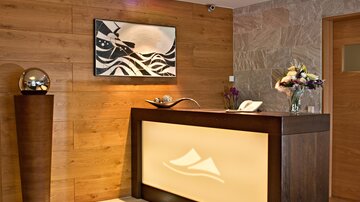 A modern hotel reception with light wood decor and stylish wall art. On the reception desk, there is a flower vase and decorative objects.